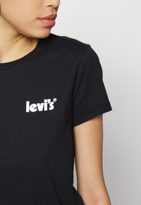 Camiseta de algodón negra con mangas cortas y cuello redondo, que presenta un logo blanco de Levi's en la parte izquierda del pecho.