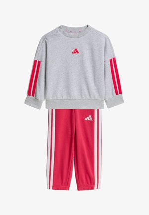 Dziecięcy dwu-częściowy strój Adidas z szarą bluzą z czerwonymi paskami na rękawach i czerwonymi spodniami z białymi paskami po bokach.