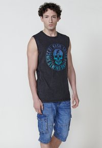 Svart ärmlös T-shirt med en blå skallegrafik och text. Kombinerad med knälånga ljusblå cargoshorts med sidofickor.