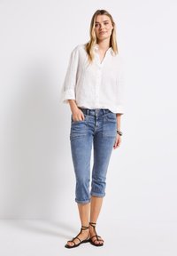 Camisa blanca de lino con botones, corte casual, mangas arremangadas; jeans de mezclilla cortos de color azul claro con bolsillos; sandalias negras de tiras.