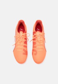 Des chaussures de sport orange vif avec une tige synthétique lisse, des accents texturés et des lacets assortis. Elles présentent une semelle intérieure rouge avec un logo.