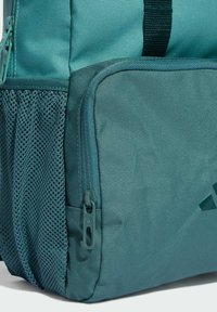Zaino verde acqua con un tessuto texturizzato, dotato di una tasca con zip e una tasca laterale in rete. Spallacci regolabili e una maniglia robusta sulla parte superiore.