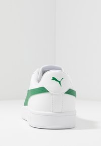 Baskets blanches avec des accents verts, dessus en cuir lisse, col rembourré et semelle en caoutchouc plate. Logo Puma visible sur le talon.