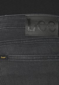 Svarta jeans i denim med en läderpatch från märket Lee på midjebandet. Har guldiga sömmar och en liten Lee-etikett nära fickan.