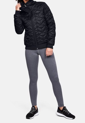 Musta tikattu takki korkealla kauluksella, vetoketjusuljenta ja resorihihansuut, yhdistettynä istuviin harmaihin legginsseihin ja mustiin urheilukengiin.