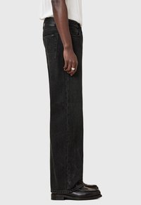 Schwarze Denim-Jeans mit geradem Bein, mittelhoher Taille, seitlichen Taschen und einem sauberen Finish. Tragen mit schwarzen Slippern.