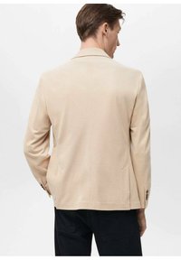 Blazer beige con colletto a soletta, spacco singolo e due tasche laterali. Texture liscia e dettagli con bottoni sui polsini delle maniche.