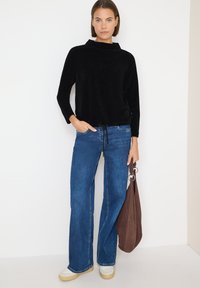 Top de pana negra con rayas verticales, combinado con jeans de campana azules y zapatillas crema. Los accesorios incluyen un bolso marrón de tipo slouchy.