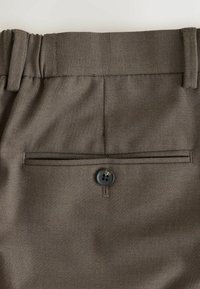Hnedé nohavice s textúrovanou látkou, rovnou pásovkou s osadením na opasok a zadným vreckom s kontrastným gombíkom.