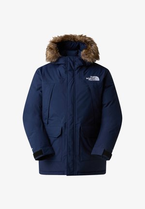 Navy blue parka jacket with a detachable faux fur hood, multiple front pockets, ribbed cuffs, and a zipper closure. Features logo on chest.