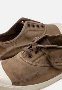 Sneaker in tela marrone con fori a occhio rotondi neri, lacci piatti e punta in gomma con suola testurizzata.