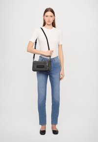 Black, textured handbag with a chain strap and logo detailing, paired with a white fitted t-shirt and light blue jeans. Simple black flats.