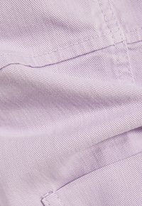 Jasnolawendowy materiał o gładkiej fakturze i diagonalnym prążkowaniu. Widoczne detale ściegów oraz kieszeń w prawym dolnym rogu.