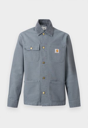 Grå arbeidsjakke med knapper, fire frontlommer, en klafflomme med knapp, Carhartt-logo på brystlommen og halsbånd i kordfløyel.