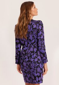 Fioletowa sukienka w kwiatowy wzór z długimi rękawami, dopasowanym krojem, szczegółowymi mankietami i gładką teksturą materiału na ciemnym tle.