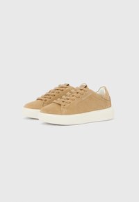 Τακούνια σουέτ σε καμηλό χρώμα με επίπεδη λευκή ελαστική σόλα, στρογγυλή μύτη και κορδόνια στον ίδιο τόνο. Διαθέτουν διακριτικές οπές στις πλευρές. Ελάχιστη σήμανση.