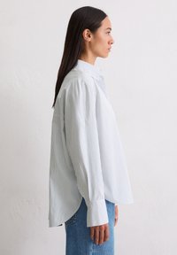 Világoskék és fehér csíkos gombos ing, laza szabással, hegyes gallérral és hosszú ujjakkal, széles mandzsettákkal.