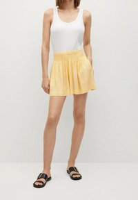 Jupe jaune avec une taille élastique, présentant un motif floral subtil. Association avec un débardeur blanc et des sandales noires à enfiler.