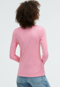 Langärmliges, pinkes Hemd aus weichem Stoff mit rundem Halsausschnitt, glatter Textur und figurbetontem Design, kombiniert mit hellblauen Jeans.