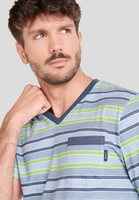 Camiseta de cuello en V a rayas en azul claro, gris y verde, con un bolsillo en el pecho adornado con un ribete azul oscuro y una etiqueta de la marca cosida. Textura de tela suave.