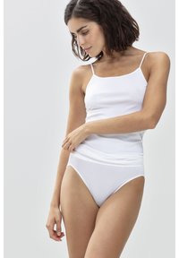 Camisola bianca con spalline sottili, texture liscia e design aderente. Abbinata a slip hipster bianchi trasparenti, con una morbida vita.