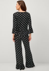 Black pajama set with white heart pattern. Top features three-quarter sleeves and flared ruffle hem. Pants are flared with matching design.
