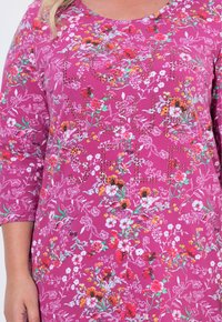 Lila bedruckte Tunika mit Dreiviertelärmeln, die ein Design aus verschiedenen Blumen und Verzierungen zwischen den Mustern zeigt.