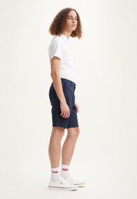Shorts bleu marine en coton, stylés avec un design classique ; associés à un t-shirt blanc et des baskets blanches.