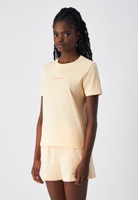 Jasno brzoskwiniowa koszulka z krótkim rękawem i okrąg�łym dekoltem, z małym haftowanym logo na klatce piersiowej oraz krótkimi spodniami w pasującym kolorze.