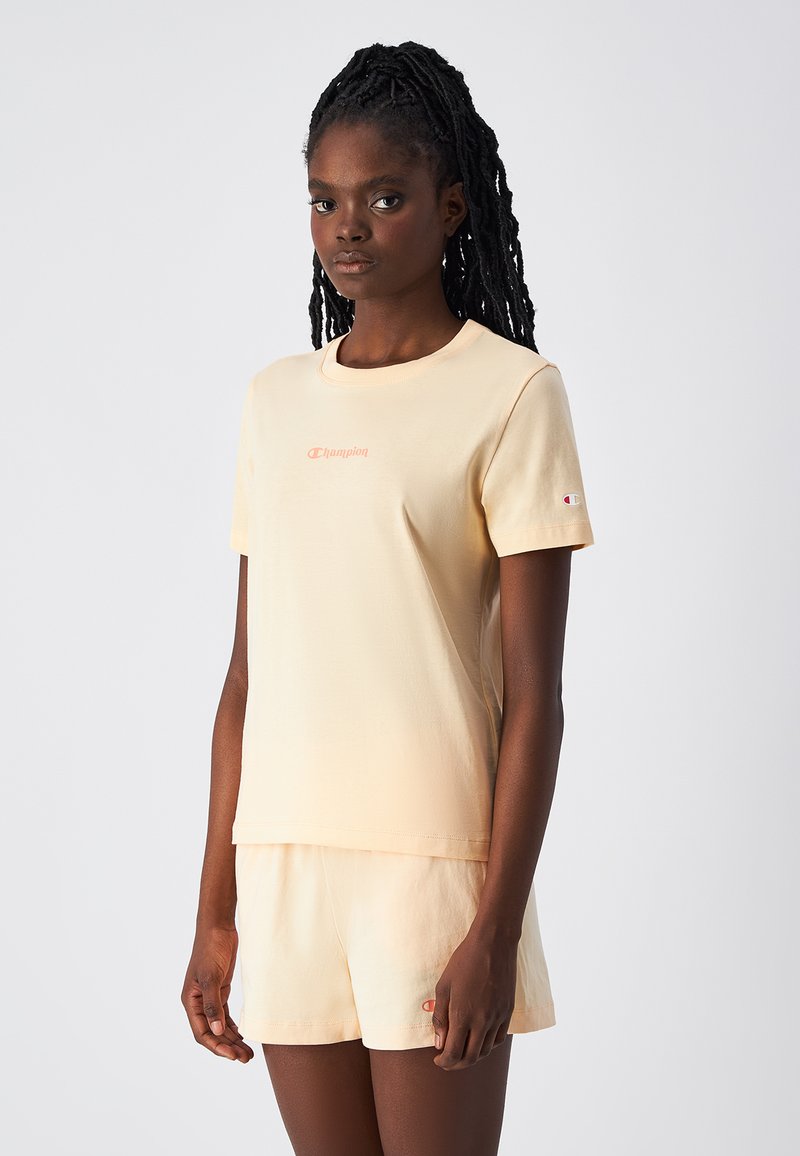 Jasno brzoskwiniowa koszulka z krótkim rękawem i okrągłym dekoltem, z małym haftowanym logo na klatce piersiowej oraz krótkimi spodniami w pasującym kolorze.