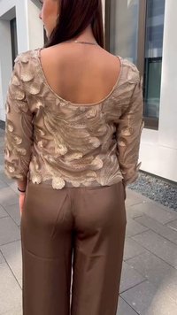 Braun bestickte Bluse mit runder Rückseite, versehen mit floralen Mustern und Dreiviertelärmeln, kombiniert mit beigen weit geschnittenen Hosen.