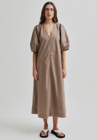 Hnědá bavlněná šaty s výstřihem do V, nafouknutými krátkými rukávy a rovnou siluetou. Design obsahuje přední zip a boční rozparky.