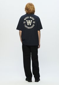 Marineblå bomulds t-shirt med grafikken "WOOD WOOD COPENHAGEN 2002" i cremefarve, med en løs pasform og korte ærmer, parret med sorte bukser.
