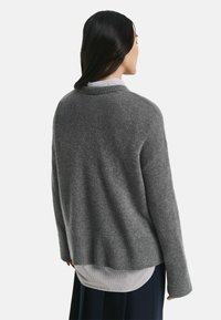 Grau wollener Pullover mit lockerer Passform, geripptem Saum und langen Ärmeln, über einem weiß-blauen gestreiften Hemd getragen. Standard-Ausschnitt.