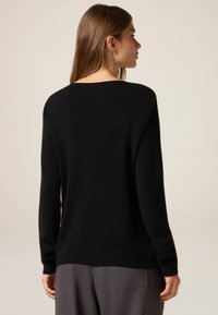 Zwarte trui met een ronde hals, lange mouwen en geribbelde boorden. Zachte textuur en een relaxte pasvorm, gecombineerd met grijze broek.