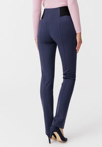 Navy stretchbroek met een hoge zwarte tailleband, slim fit ontwerp, gladde textuur en taps toelopende pijpen, gecombineerd met hoge hakken.