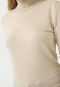 Pull à col roulé beige en tissu doux et léger. Présente une coupe ajustée avec une texture lisse et un col côtelé.