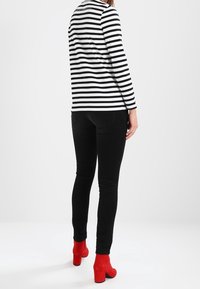 Gestreept zwart-wit shirt met lange mouwen, gecombineerd met aansluitende zwarte jeans en felrode enkellaarsjes met blokhak, gezien van achteren.