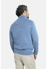 Suéter de punto azul con un cuello alto. Presenta puños y dobladillo acanalados, textura suave y detalles de costura elevados en la parte posterior.