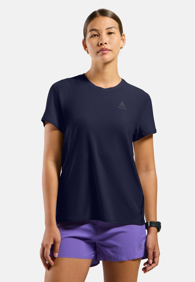 Marineblauwe korte mouw t-shirt van lichtgewicht stof, met een ronde halslijn en subtiele logo. Gecombineerd met paarse shorts.