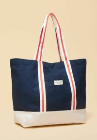 Tumesinine kandekott valge põhjaga, punaste ja valgete triibuliste käepidemetega ning ees väike silt tekstiga "Joules".