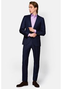 Granatowy garnitur o slim fit, stylizowany z jasnofioletową koszulą. Posiada subtelny wzór, jednorzędową marynarkę i ciemno-brązowe zamszowe buty.