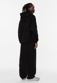 Felpa nera oversize e pantaloni della tuta abbinati in tessuto morbido, con cappuccio e vestibilità rilassata, abbinati a sneakers grigie chiare.