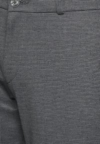 Grå mönstrad tyger av byxor med en subtil rutdesign. Har en knapp och en skräddarsydd midja, med en slät yta.