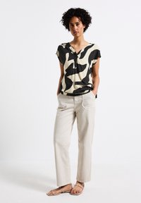 Blusa a fantasia nera e crema con scollo a V e bottoni, abbinata a pantaloni beige chiaro e sandali beige con cinturini. Tessuto dalla texture liscia.
