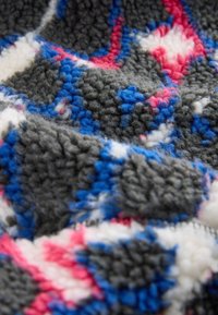 Tissu en polaire gris avec une surface texturée et duveteuse présentant un motif géométrique multicolore en tons bleu, blanc et rouge.