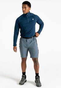 Dunkelblauer Langarmpullover mit halbem Reißverschluss, kombiniert mit grauen Cargo-Shorts mit seitlichen Taschen und einem schwarzen Gürtel. Graue Wanderschuhe runden den Look ab.