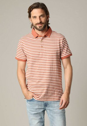 Polo rayé en terre cuite et blanc, avec un col, une patte de boutonnage à trois boutons et des manches courtes, porté avec un jean bleu clair.