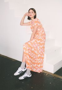 Maxi sukienka w pomarańczowy i różowy abstrakcyjny wzór; krótkie rękawy; zestawiona z szarymi skarpetami i białymi sneakerami z czarnymi akcentami.