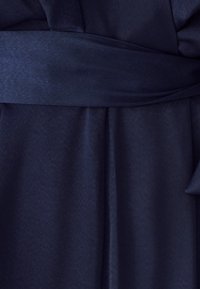 Navy blauwe wikkeljurk gemaakt van zachte stof. Beschikt over een brede riem op de taille en geplooide details, wat zorgt voor een gladde textuur en elegante val.